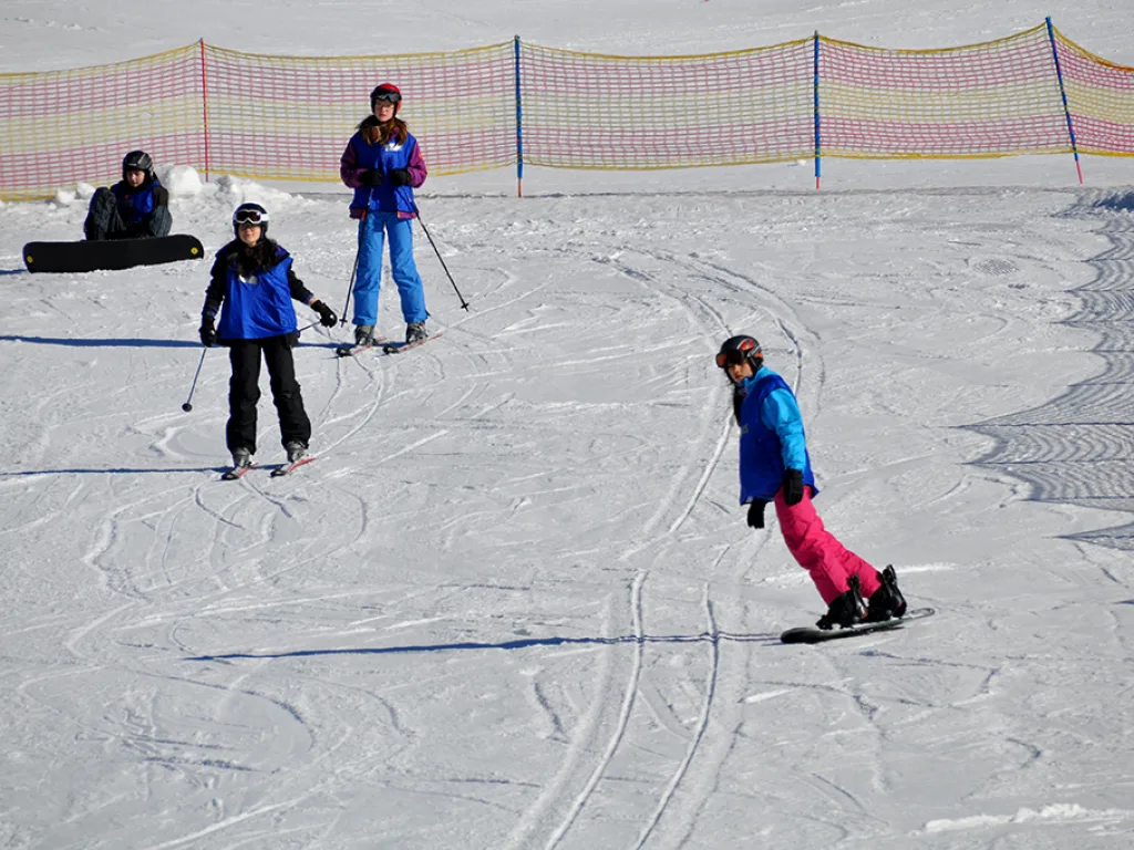 Snowboarderin und zwei Skifahrer üben nebeneinander am Hang.